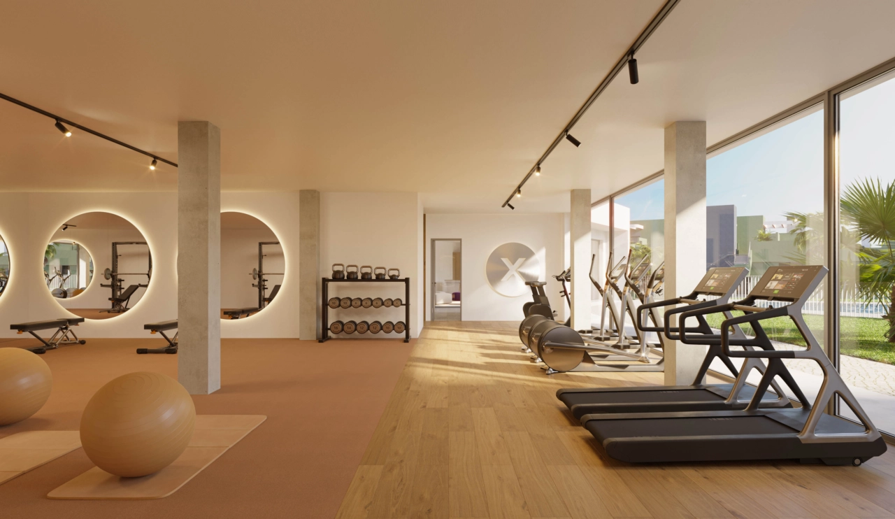 Et fullt utstyrt treningsstudio med store vinduer som vender ut mot hagene og bassengområdet.