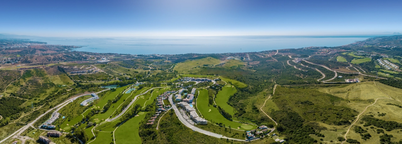En vidstrakt flyfoto av Sunny Golf-prosjektet, perfekt integrert med de frodige, grønne fairwayene på Estepona Golf og det glitrende Middelhavet i bakgrunnen.